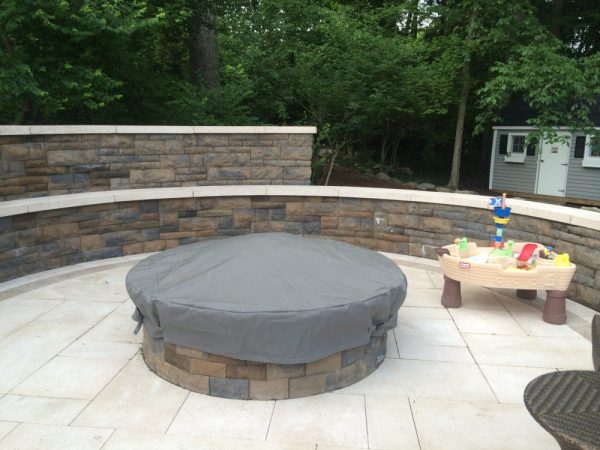 Round firepit on a patio with a black fabric cover over it to protect it from the elements