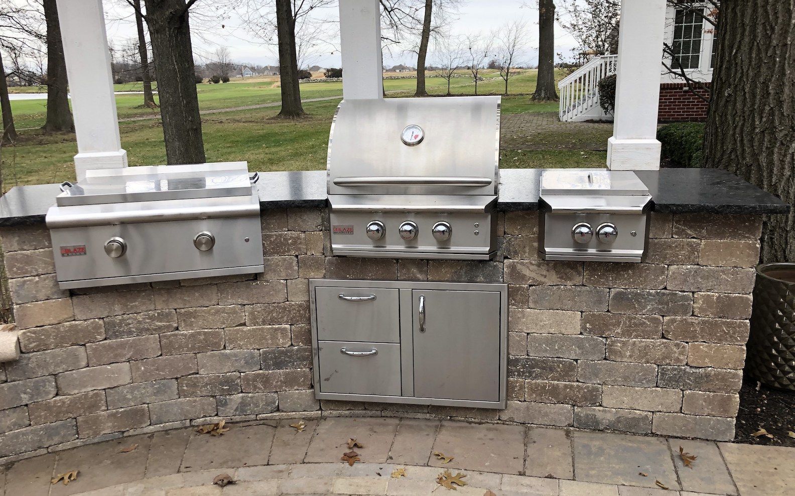 Outdoor kitchen with a stainless steel grill, burners, and sink set on a stone counter.